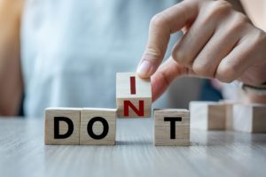 Business man hand holding wooden cube with flip over block DON T to DO IT word on table background