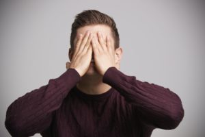 Portrait of a young white man with hands covering his face