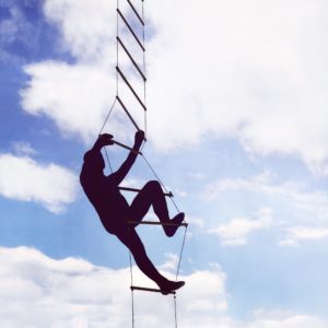 Silhouette of a man climbing a rope ladder into the sky